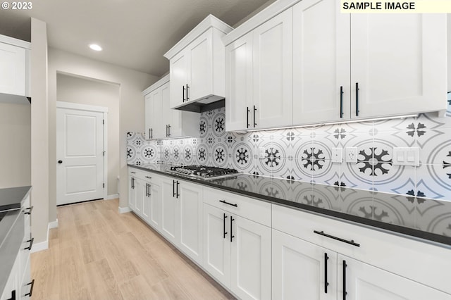 kitchen with stainless steel gas stovetop, light hardwood / wood-style floors, tasteful backsplash, and white cabinetry