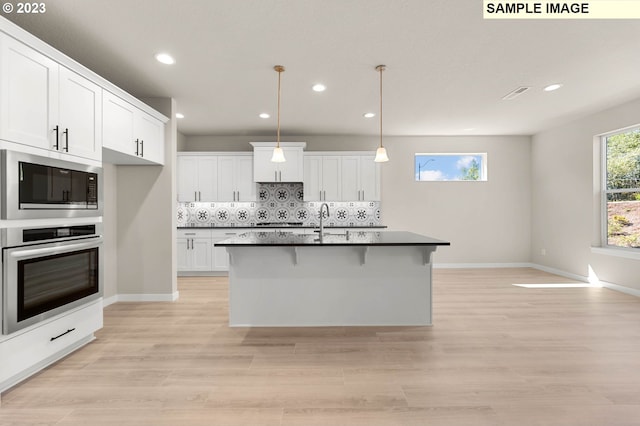 kitchen with decorative light fixtures, a kitchen island with sink, white cabinetry, appliances with stainless steel finishes, and decorative backsplash