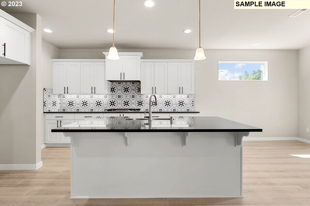 kitchen featuring light wood-type flooring, white cabinetry, a center island with sink, and hanging light fixtures