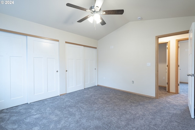 unfurnished bedroom with two closets, dark carpet, ceiling fan, and lofted ceiling