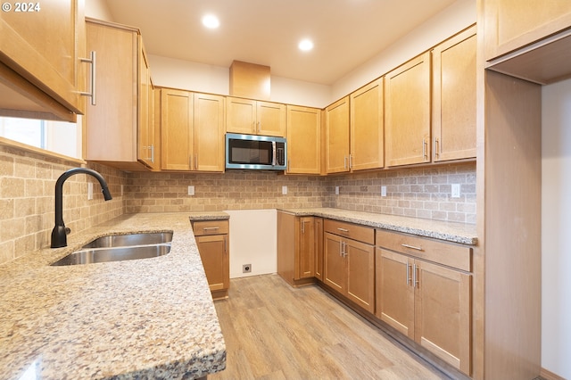 kitchen featuring backsplash, light stone countertops, sink, and light wood-type flooring