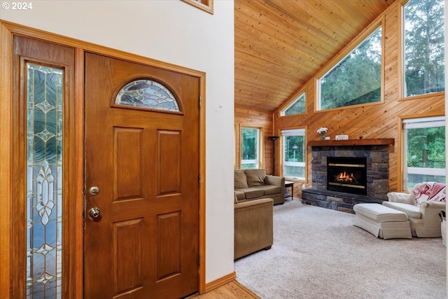 interior space with high vaulted ceiling, a stone fireplace, wooden ceiling, light carpet, and wooden walls