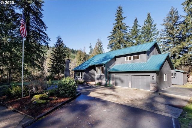 view of front of house with driveway, stone siding, a garage, and metal roof