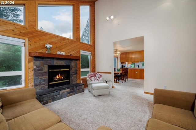 carpeted living room featuring a towering ceiling, wooden walls, and a stone fireplace