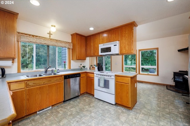 kitchen featuring a wood stove, sink, kitchen peninsula, light tile patterned flooring, and white appliances