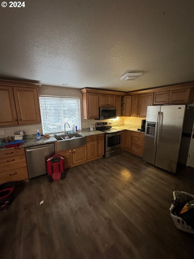 kitchen featuring dark wood-type flooring, sink, light stone countertops, a textured ceiling, and appliances with stainless steel finishes