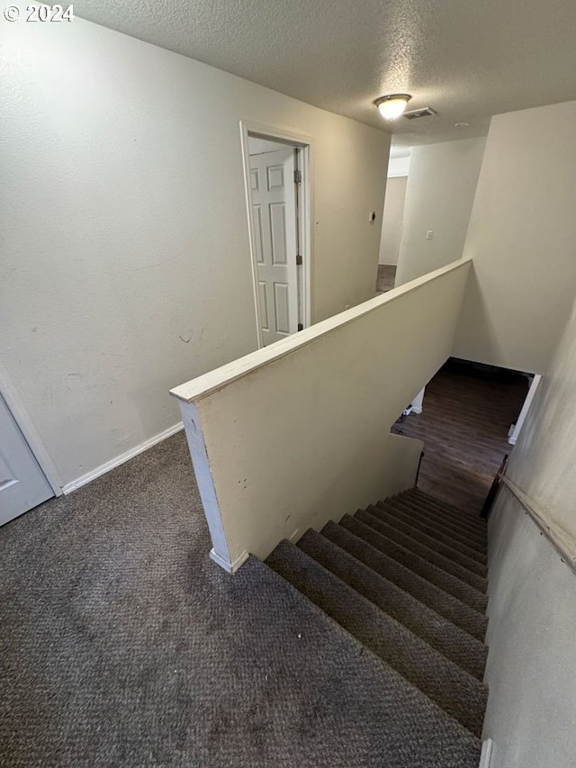 stairway with carpet and a textured ceiling