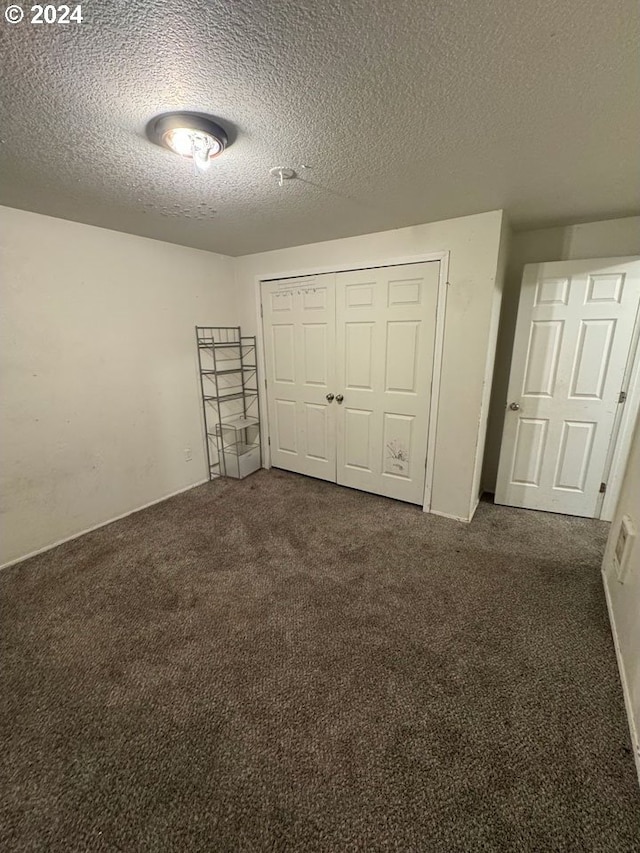 unfurnished bedroom featuring dark colored carpet, a textured ceiling, and a closet