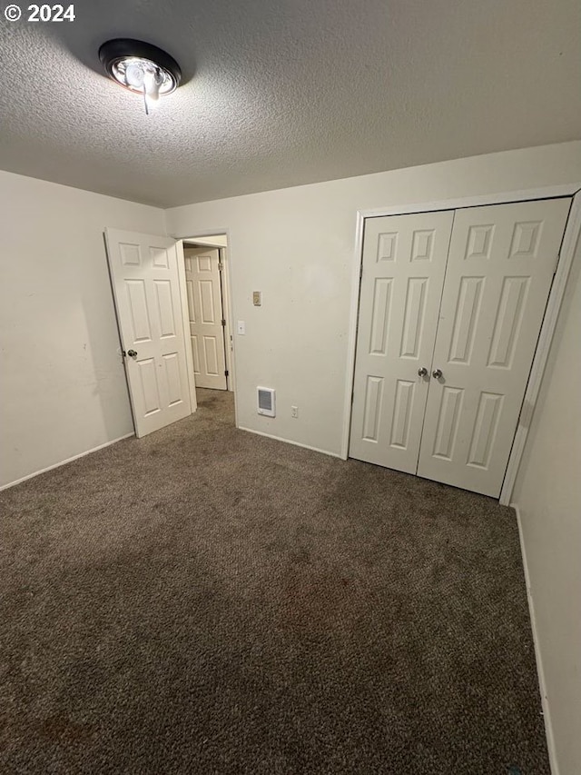 unfurnished bedroom featuring dark colored carpet, a textured ceiling, and a closet