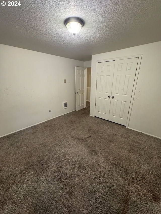 unfurnished bedroom with a closet, dark carpet, and a textured ceiling