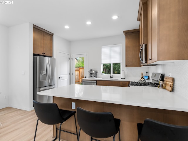 kitchen featuring stainless steel appliances, a sink, a peninsula, light countertops, and light wood-type flooring