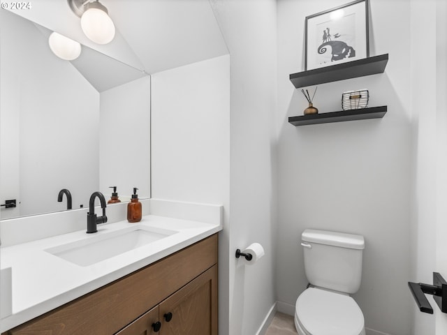 half bathroom with vanity, toilet, lofted ceiling, and baseboards