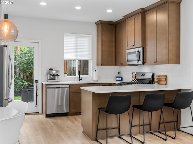 kitchen featuring a kitchen breakfast bar, sink, hanging light fixtures, light wood-type flooring, and appliances with stainless steel finishes