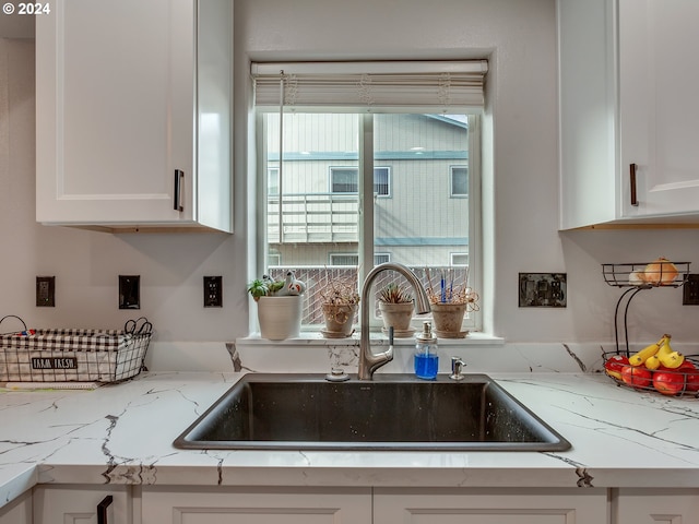 kitchen featuring light stone countertops, white cabinetry, and sink