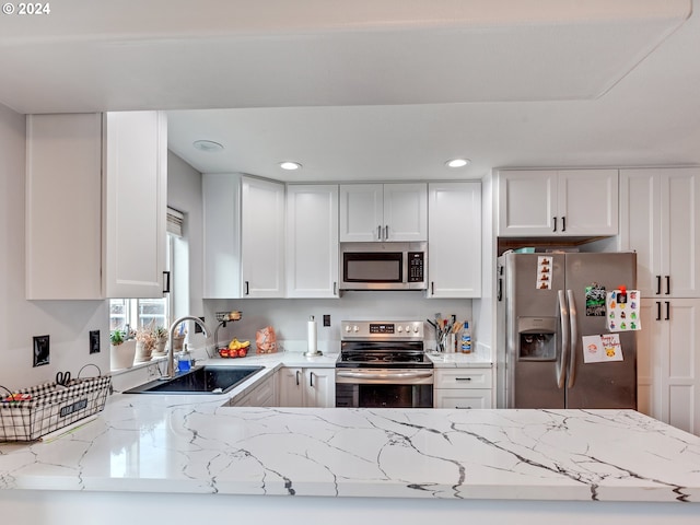 kitchen featuring white cabinets, kitchen peninsula, sink, appliances with stainless steel finishes, and light stone countertops