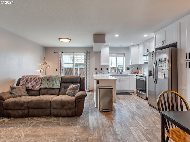 kitchen featuring light wood-type flooring, sink, stainless steel appliances, light stone countertops, and white cabinets