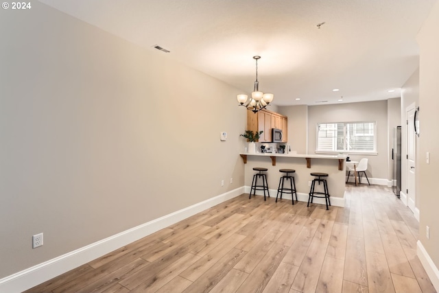 kitchen with light brown cabinets, a kitchen breakfast bar, a notable chandelier, light hardwood / wood-style floors, and kitchen peninsula