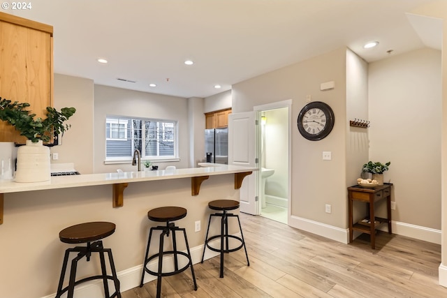 kitchen featuring kitchen peninsula, stainless steel fridge with ice dispenser, a breakfast bar area, and light hardwood / wood-style flooring