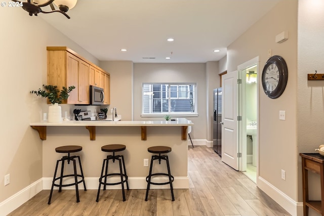 kitchen featuring light brown cabinetry, stainless steel appliances, a breakfast bar area, and light hardwood / wood-style floors