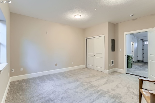 unfurnished bedroom with a textured ceiling, electric panel, light colored carpet, and a closet