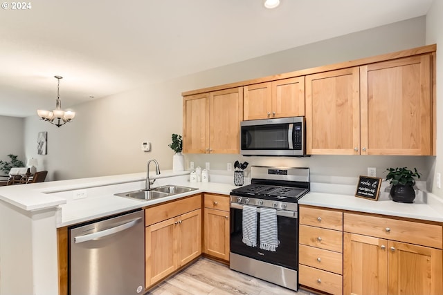 kitchen featuring kitchen peninsula, appliances with stainless steel finishes, sink, light hardwood / wood-style flooring, and an inviting chandelier