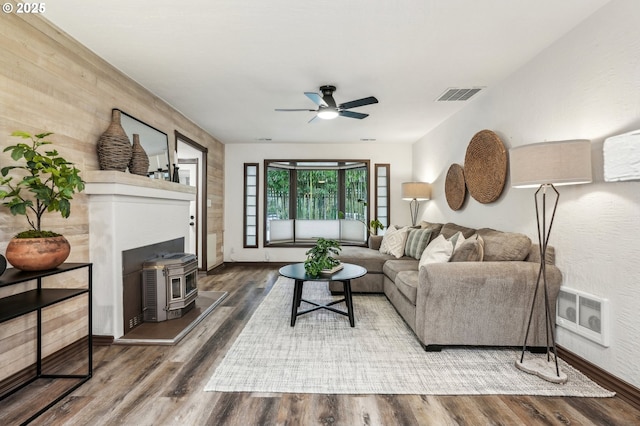 living room with ceiling fan, a wood stove, and hardwood / wood-style flooring