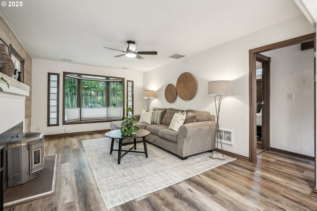 living room with ceiling fan, a wood stove, and hardwood / wood-style floors