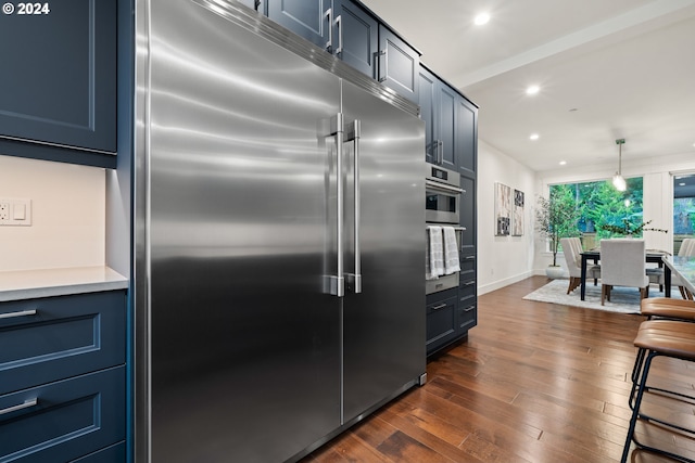 kitchen with blue cabinetry, dark wood-type flooring, stainless steel built in fridge, and hanging light fixtures