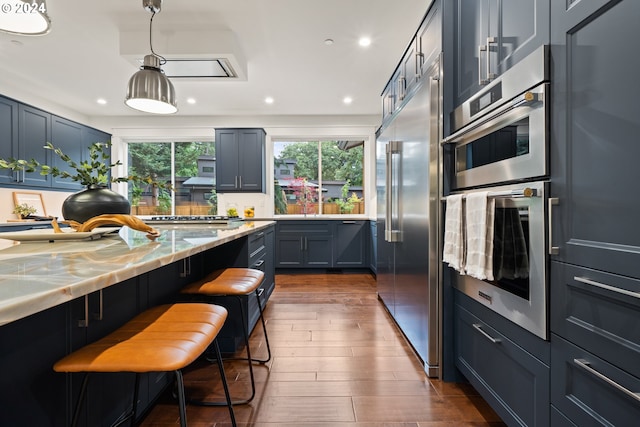 kitchen featuring light stone counters, dark hardwood / wood-style floors, decorative light fixtures, a kitchen bar, and appliances with stainless steel finishes