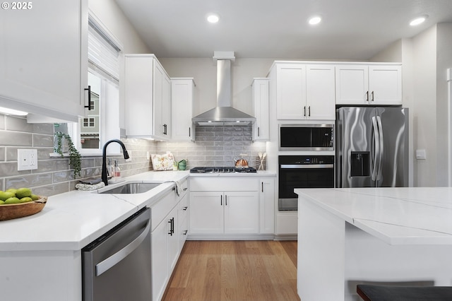 kitchen featuring stainless steel appliances, white cabinetry, sink, and wall chimney range hood