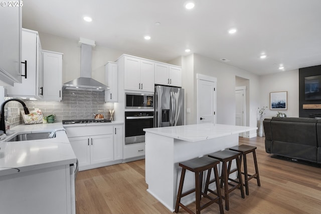 kitchen featuring sink, appliances with stainless steel finishes, white cabinets, a kitchen island, and wall chimney exhaust hood