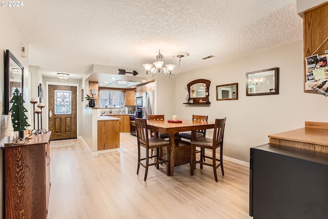 dining area with light hardwood / wood-style flooring, a notable chandelier, and a textured ceiling