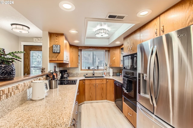 kitchen with black appliances, light stone counters, sink, light hardwood / wood-style floors, and a tray ceiling