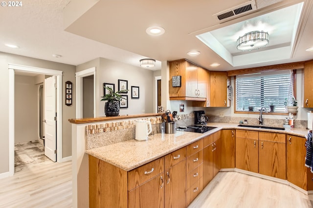 kitchen featuring black electric cooktop, sink, light stone countertops, a tray ceiling, and light wood-type flooring