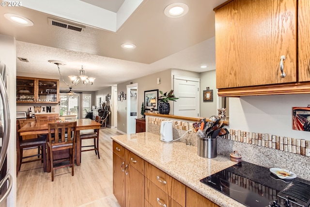 kitchen featuring black electric cooktop, light stone countertops, a textured ceiling, hanging light fixtures, and light wood-type flooring