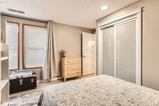 bedroom featuring light wood-type flooring, a textured ceiling, and a closet