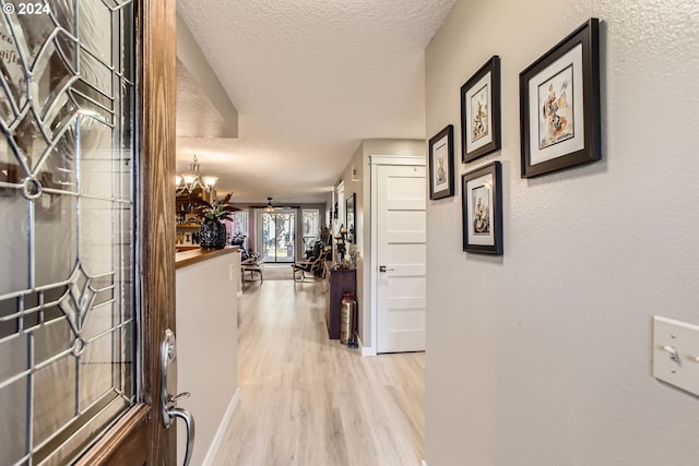 hallway featuring a chandelier, a textured ceiling, and light wood-type flooring