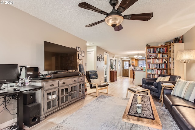 living room with ceiling fan with notable chandelier, light hardwood / wood-style floors, and a textured ceiling