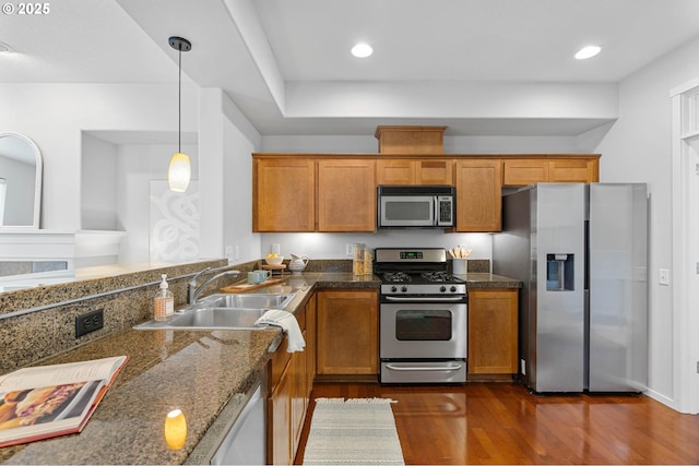 kitchen featuring dark wood-type flooring, sink, decorative light fixtures, dark stone countertops, and appliances with stainless steel finishes