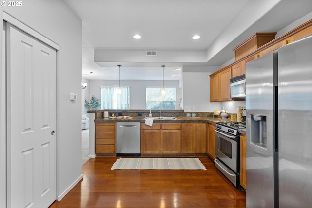 kitchen featuring sink, dark wood-type flooring, stainless steel appliances, decorative light fixtures, and kitchen peninsula