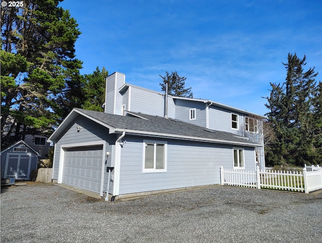 exterior space with an outbuilding, a garage, a shingled roof, fence, and a chimney