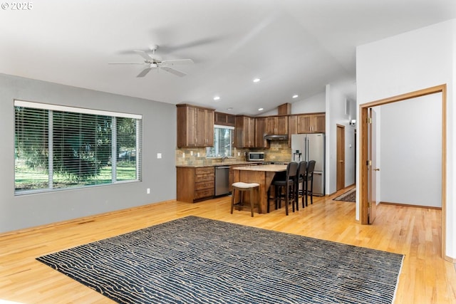 kitchen with ceiling fan, stainless steel appliances, a kitchen bar, decorative backsplash, and light wood-type flooring