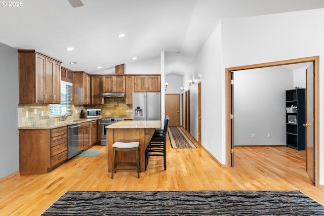 kitchen with backsplash, light hardwood / wood-style flooring, a kitchen island, a kitchen bar, and stainless steel appliances