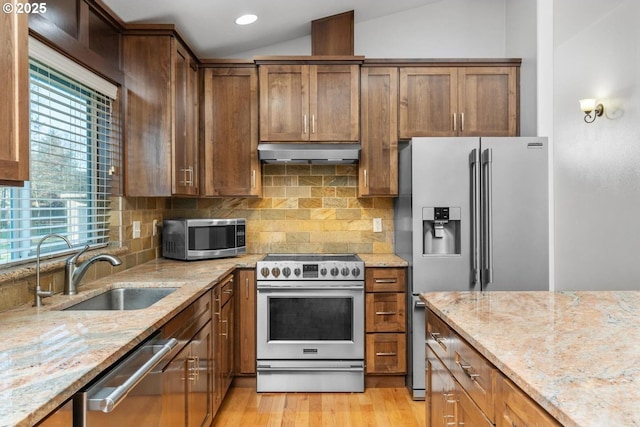 kitchen featuring light stone countertops, appliances with stainless steel finishes, a wealth of natural light, vaulted ceiling, and sink