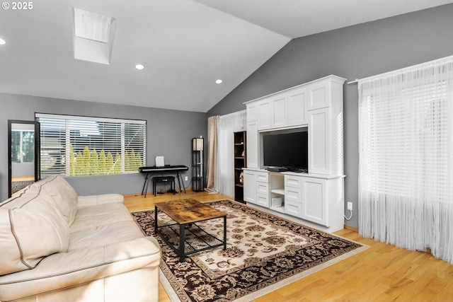 living room featuring vaulted ceiling with skylight and light hardwood / wood-style floors