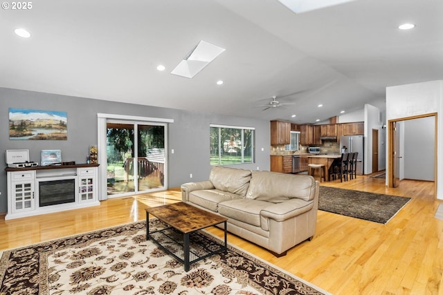 living room with light hardwood / wood-style floors, lofted ceiling with skylight, and ceiling fan