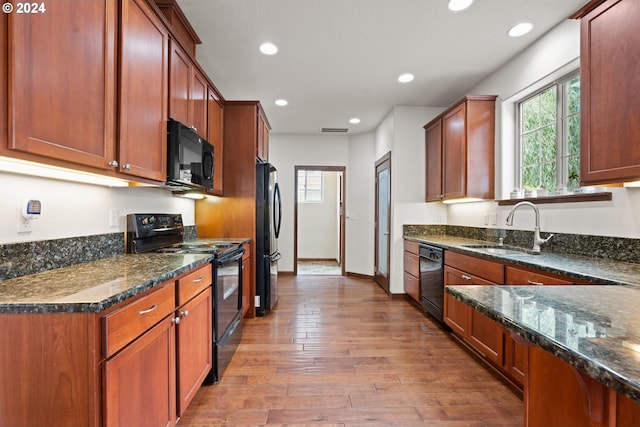 kitchen with dark stone counters, light hardwood / wood-style flooring, black appliances, and sink