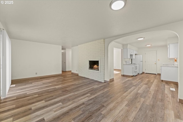 18765 SW Kinnaman Rd, Beaverton, OR 97078 - unfurnished living room featuring light wood-type flooring, a sink, arched walkways, and a fireplace