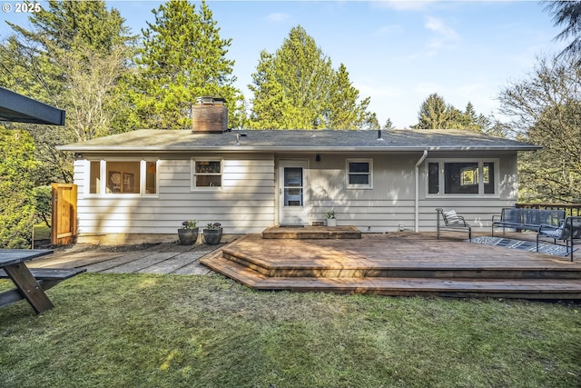 back of property with a chimney, a lawn, and a deck