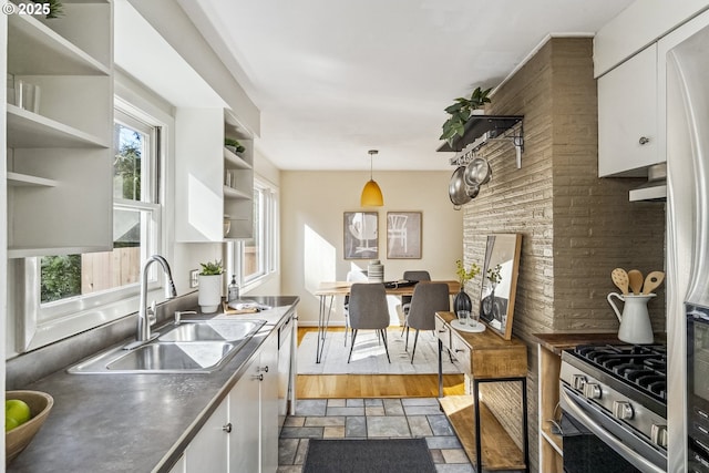 kitchen with stone finish flooring, stainless steel appliances, white cabinetry, open shelves, and a sink